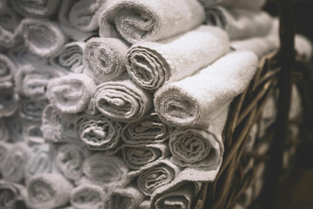 Stack of neatly rolled white towels in a woven basket, perfect for spa or bathroom settings.